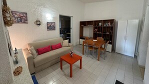 Un salon avec un canapé, une table basse et une table à manger avec des chaises. On aperçoit une cuisine au fond.