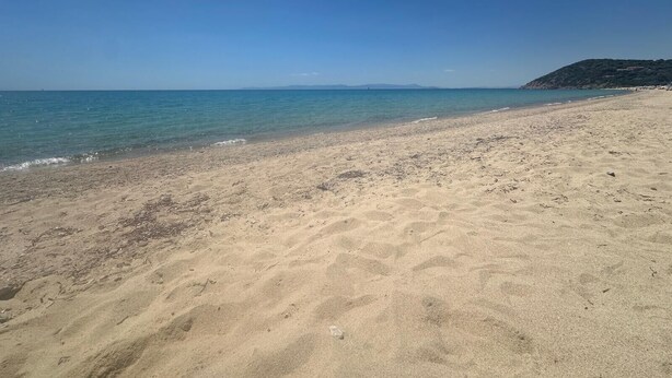 Une plage de sable fin, avec une eau d’un bleu limpide et une montagne qui se dessine à l’horizon.
