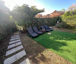 Un jardin avec un espace aménagé pour s’asseoir à l’extérieur, un sentier et une pelouse.