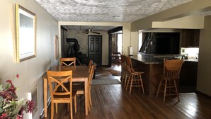 Un comedor con sillas de madera y una mesa, una cocina con barra y un ventilador de techo.