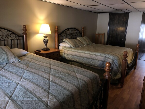 Una habitación de hotel con dos camas, una mesita de noche con lámpara y suelo de madera.
