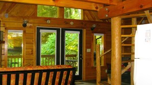 A wooden cabin interior with a dining table, two doors leading outside, and a staircase.