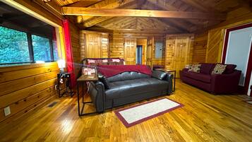 A wooden cabin interior with a leather sofa, a red couch, and a wooden floor.