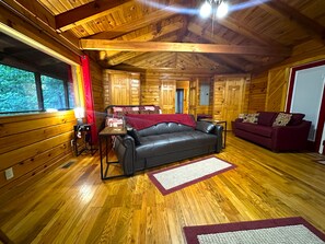 A wooden cabin interior with a leather sofa, a red couch, and a wooden floor. - Cozy secluded cabin with rock overhand and Wi-Fi (Rogers)