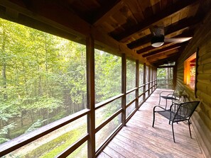 Una cabaña de madera con porche cubierto, ventanas grandes y vistas al bosque.
