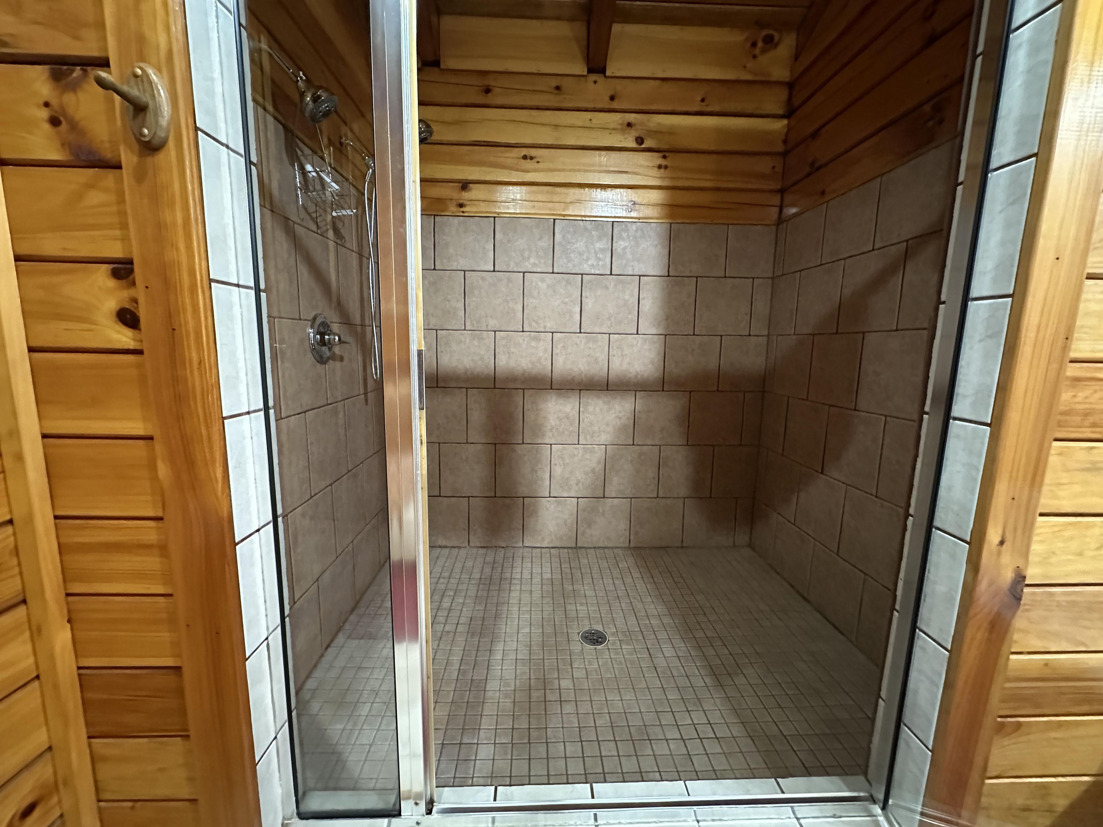 Une salle de douche aux murs recouverts de carreaux et dotée d’une porte en métal, dont les murs sont lambrissés en bois.