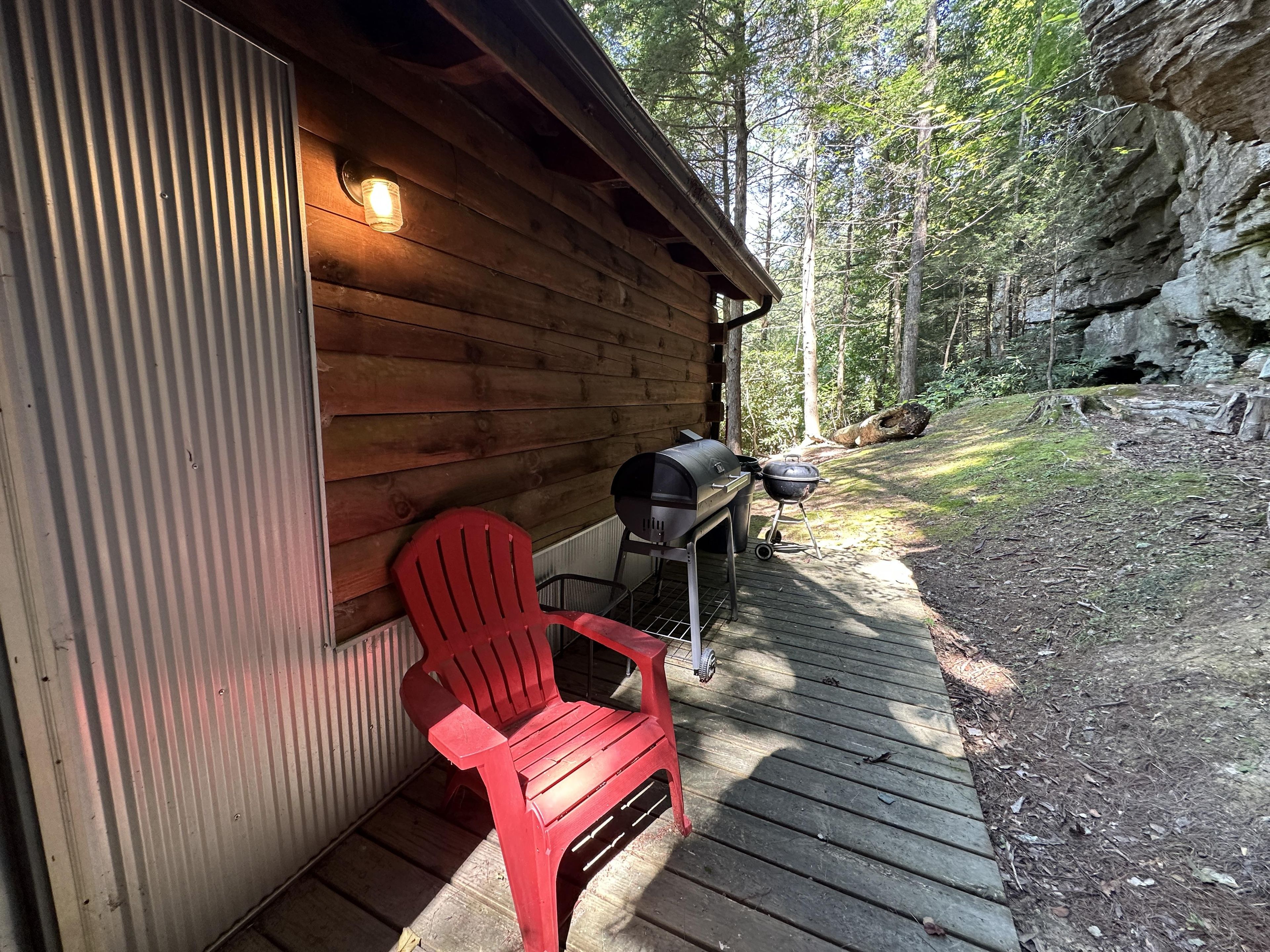 Une cabane en bois avec une chaise rouge et un barbecue à l’extérieur.