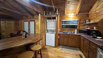 A compact kitchen with wooden cabinets, a bar area with stools, a refrigerator, and a microwave.
