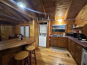Eine kompakte Küche mit Holzausstattung, einer Bar mit Hockern, einem Kühlschrank und einer Mikrowelle.