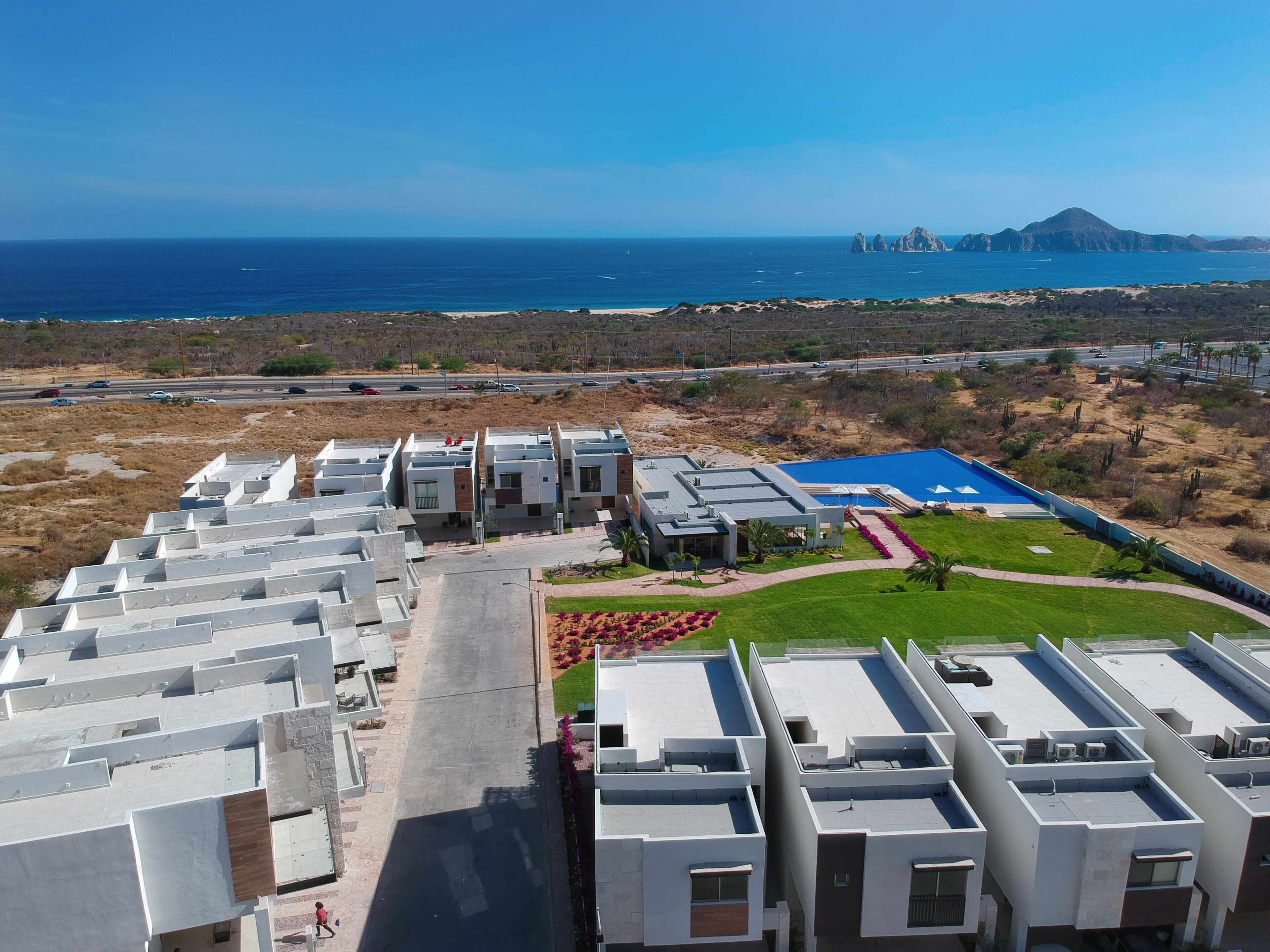 A modern residential complex with multiple apartment buildings, a swimming pool, and a view of the ocean.