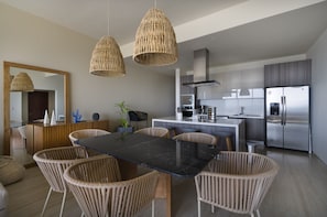 A modern kitchen with a dining area, featuring wicker chairs, a black marble table, and stainless steel appliances. - NEW CONDO 3BR/3BTH with arch view at Vista Vela condos (Cabo San Lucas)