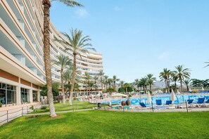 Un hotel con zona de piscina, palmeras y cielo despejado.