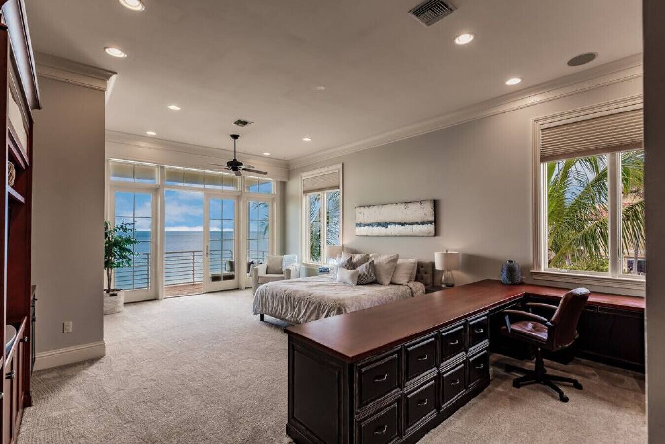 A spacious bedroom with a large bed, a desk, and a view of the ocean through large windows.
