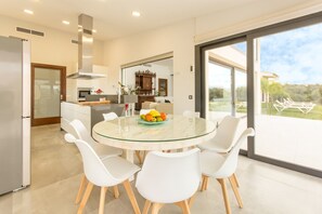 Une cuisine moderne avec une table à manger en verre, des chaises blanches et une vue sur l’extérieur.