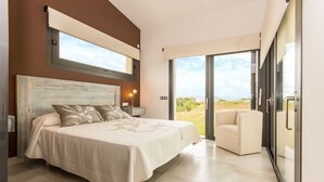 Une chambre à coucher comprenant un lit, une table de chevet, une chaise, une grande fenêtre et une porte-fenêtre coulissante donnant sur un balcon.