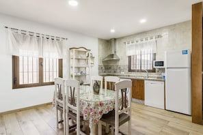 Cozinha com mesa de jantar, cadeiras, geladeira, micro-ondas e painel de azulejos.