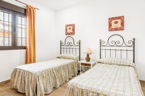 Une chambre avec deux lits simples, une petite table de chevet avec une lampe et une fenêtre avec des rideaux.