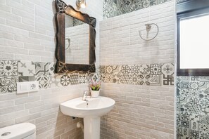 Une salle de bain avec un lavabo blanc, un miroir et des carreaux à motifs.