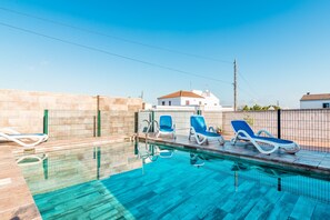 Une piscine avec des chaises longues, un mur de pierre et un bâtiment en arrière-plan.