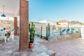 Un espace extérieur aménagé en terrasse, avec une piscine, des chaises longues et des plantes en pot.