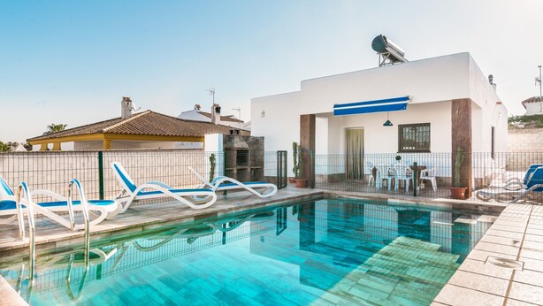 En swimmingpool med solstolar, en liten byggnad med ett blått markis och en satellantenn.