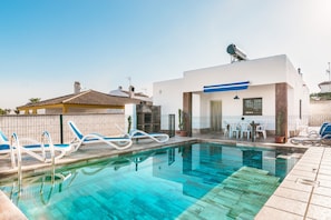 Uma piscina com espreguiçadeiras, um pequeno edifício com toldo azul e uma antena parabólica.