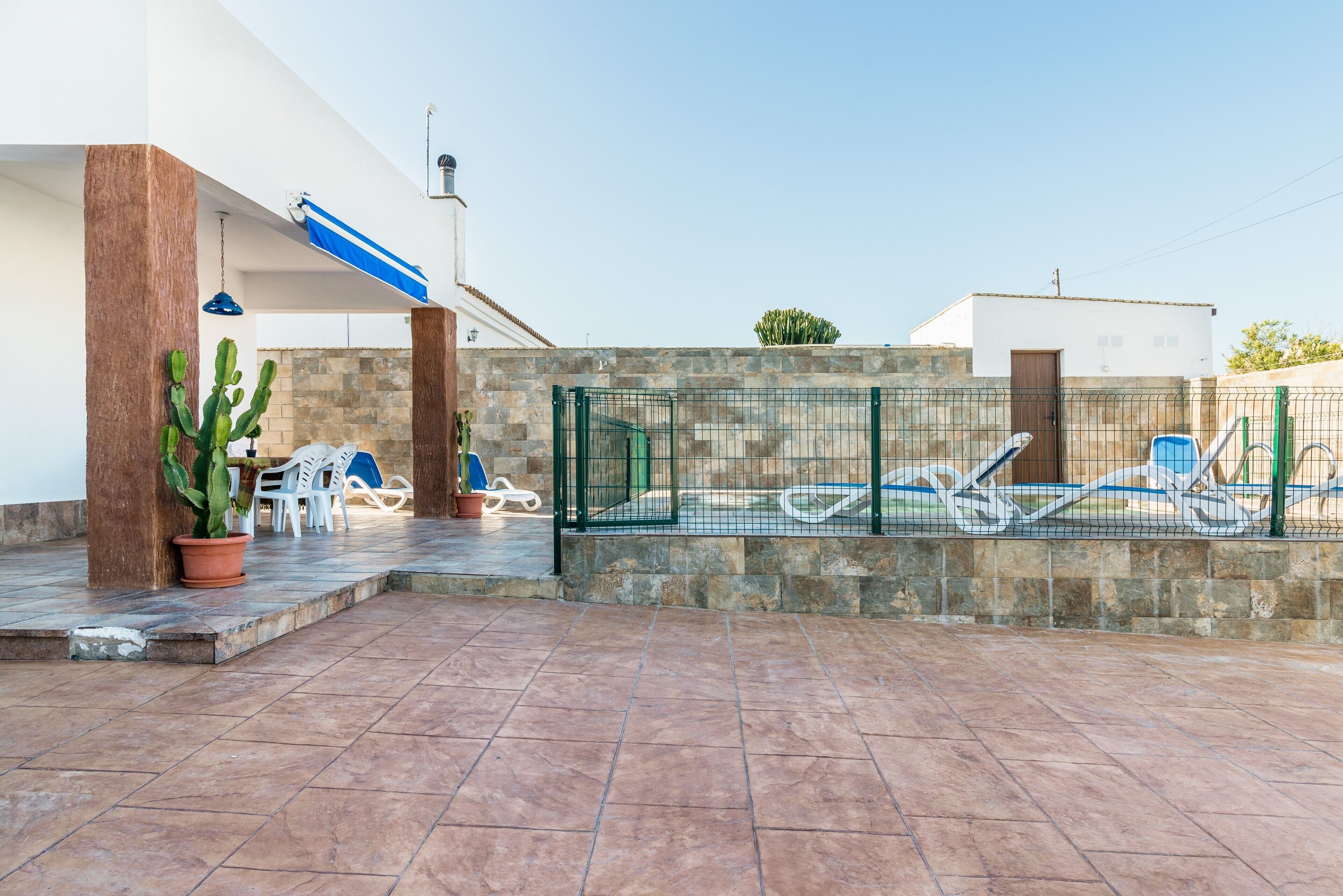 Eine Terrasse mit Kakte, Stühlen, einem Pool und einem Zaun.