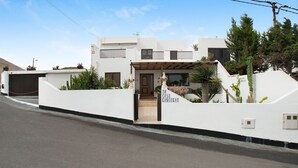 Une maison moderne à deux étages, dotée d’un porche, d’un garage et d’un jardin bien entretenu où l’on trouve des cactus et d’autres plantes.