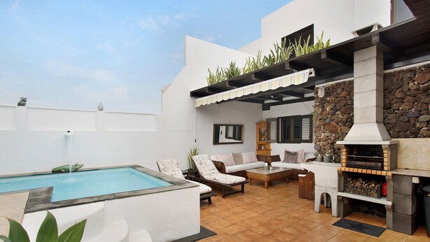 Une piscine avec des chaises longues, un mur en pierre et un espace barbecue.