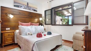 Une chambre à coucher avec une tête de lit en bois, un lit avec une literie blanche, une table de chevet, une commode, une fenêtre donnant sur un beau paysage et une lampe fixée au mur.