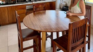 Una mesa de comedor de madera con sillas, una zona de cocina con microondas, estufa y fregadero, y una lámpara colgante.
