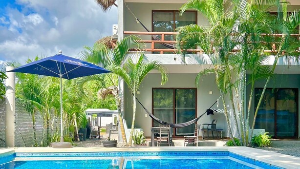 Una piscina con agua cristalina azul, rodeada por un edificio moderno con balcones y palmeras.