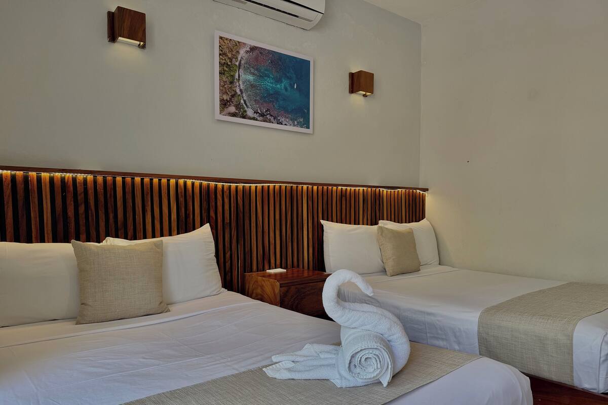 A hotel room with two beds, a wooden headboard, a wall-mounted air conditioner, and a framed picture.