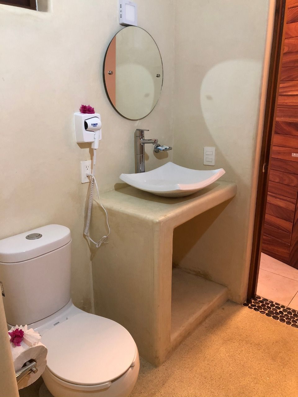 Un baño pequeño con inodoro, lavamanos, espejo y secador de pelo en la pared.
