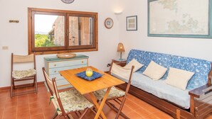 Une pièce avec une table en bois, des chaises, un canapé, une fenêtre donnant sur un paysage agréable, une carte accrochée au mur et une petite lampe.