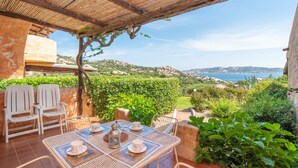 Une terrasse extérieure avec une table dressée pour deux personnes, des chaises et une vue sur la mer.