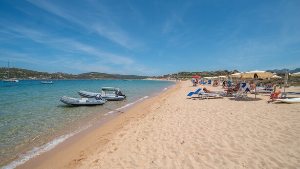 Une plage avec une eau cristalline, des bateaux et des chaises longues.