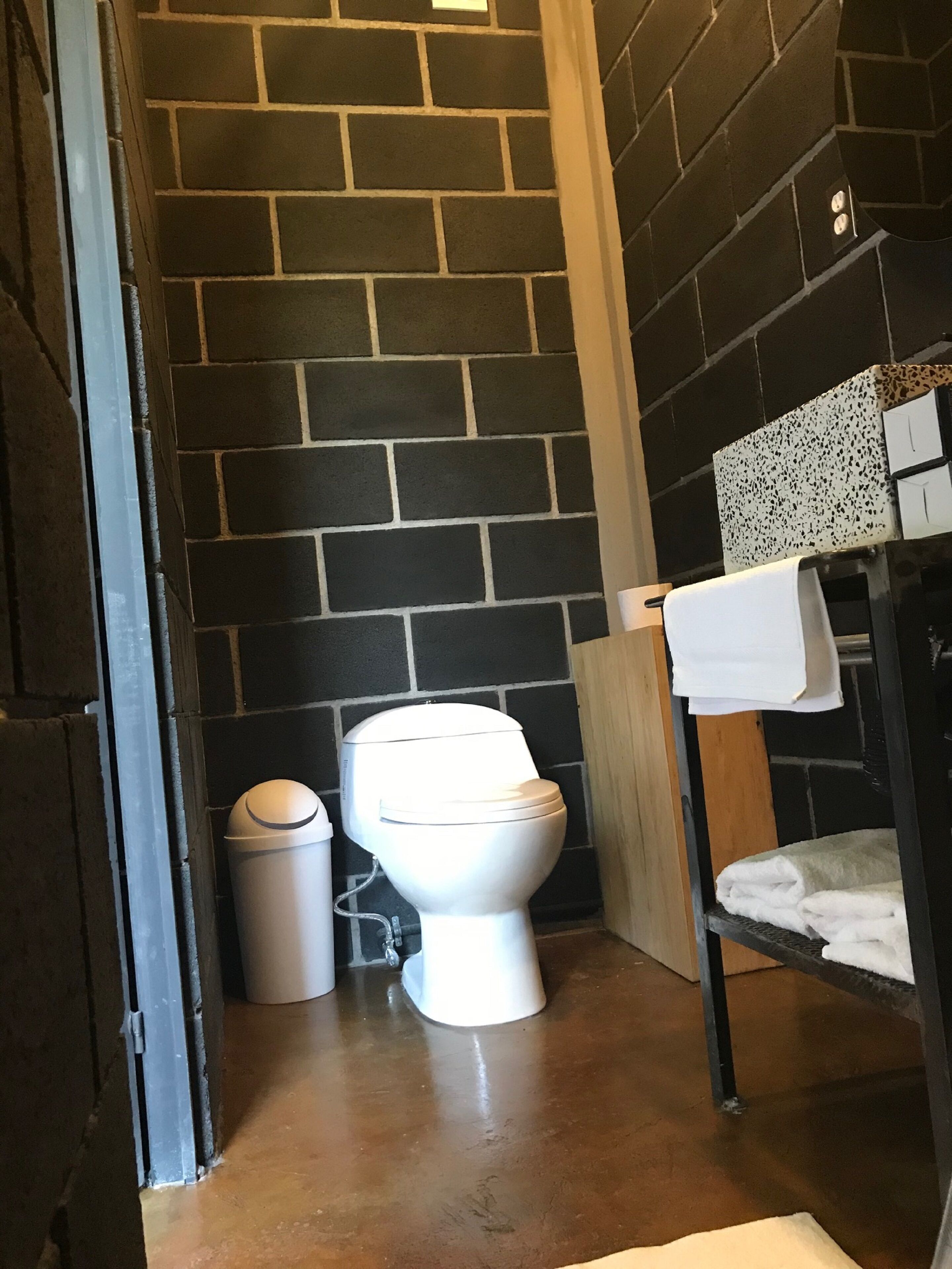 Un baño con un inodoro blanco, un cubo de basura y un perchero con toallas dobladas.