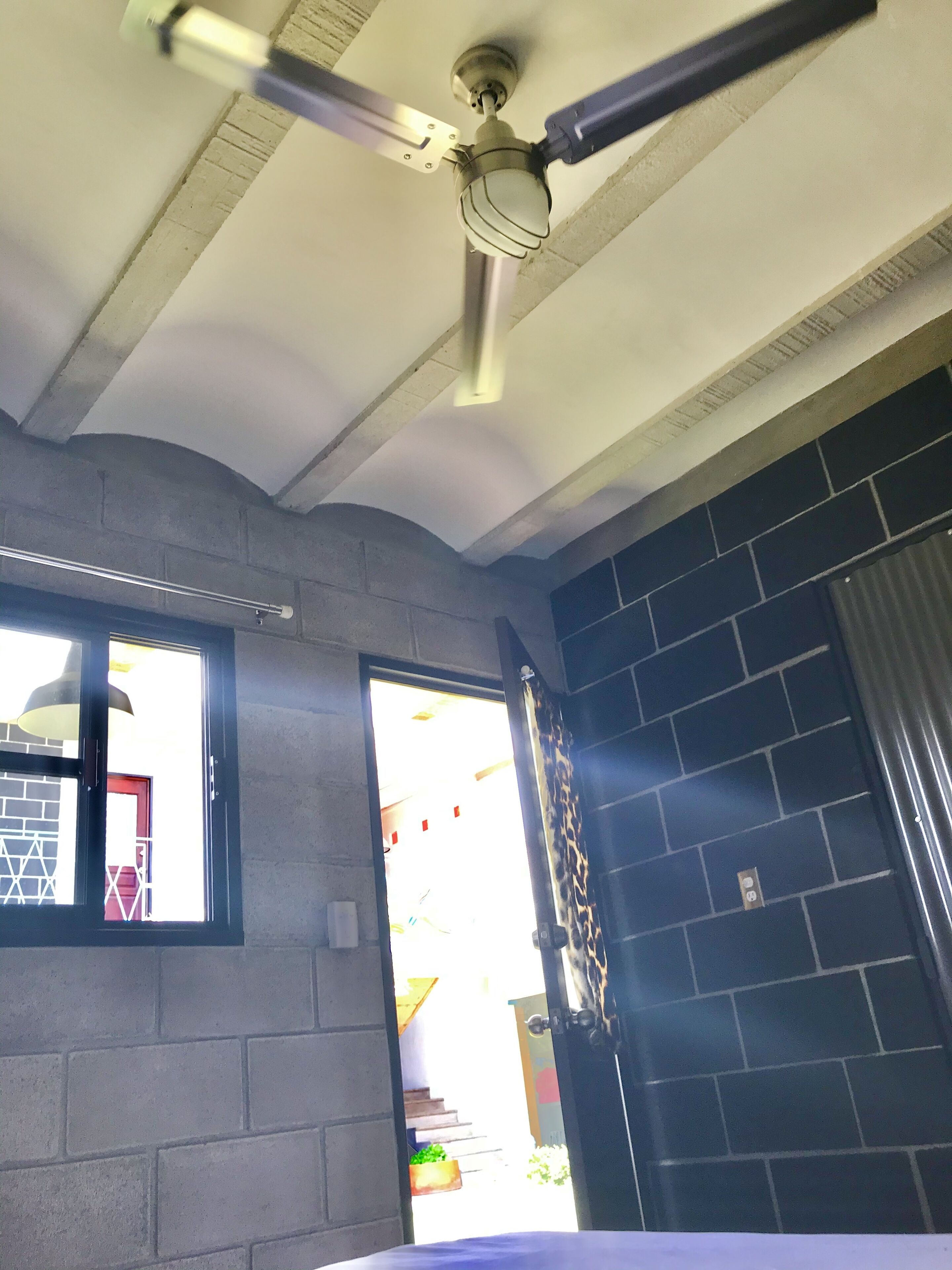 Quarto com ventilador de teto, janela com vista e porta para o exterior.