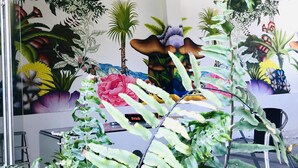 Een kamer met een muurschildering van tropische planten en bloemen, een ladder en een stoel.