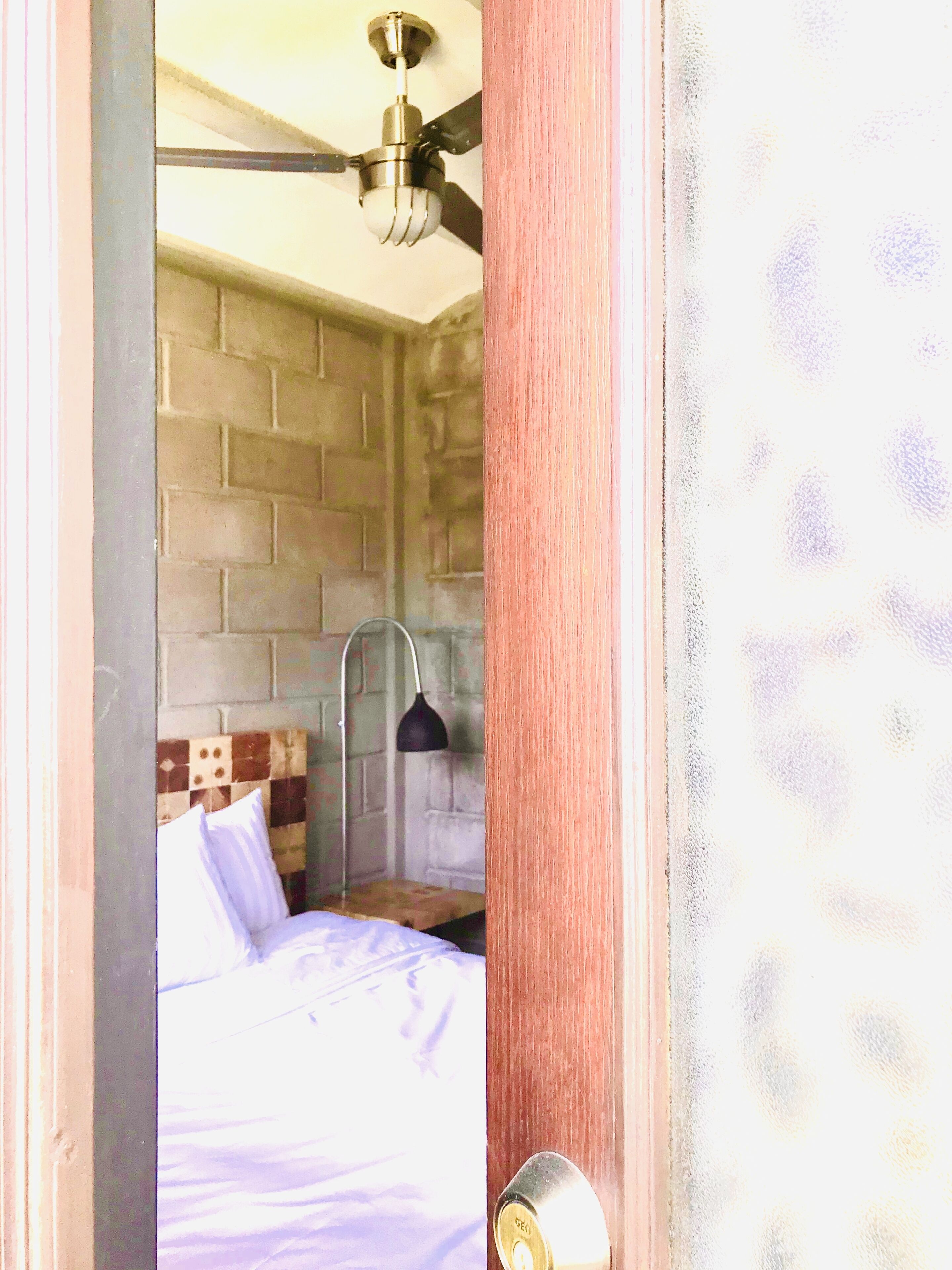 Una habitación con cama, ventilador de techo y pared de ladrillo.