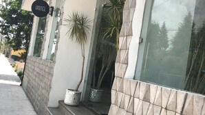 Een hotelentree met een bord, plantenbakken en een gevel betegeld met tegels.
