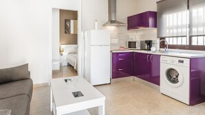 Een kleine keuken met een wasmachine, een eethoek met een tafel, en een bank.