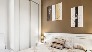 Een slaapkamer met een bed, nachtkastjes, een lamp en twee kunstwerken aan de muur.