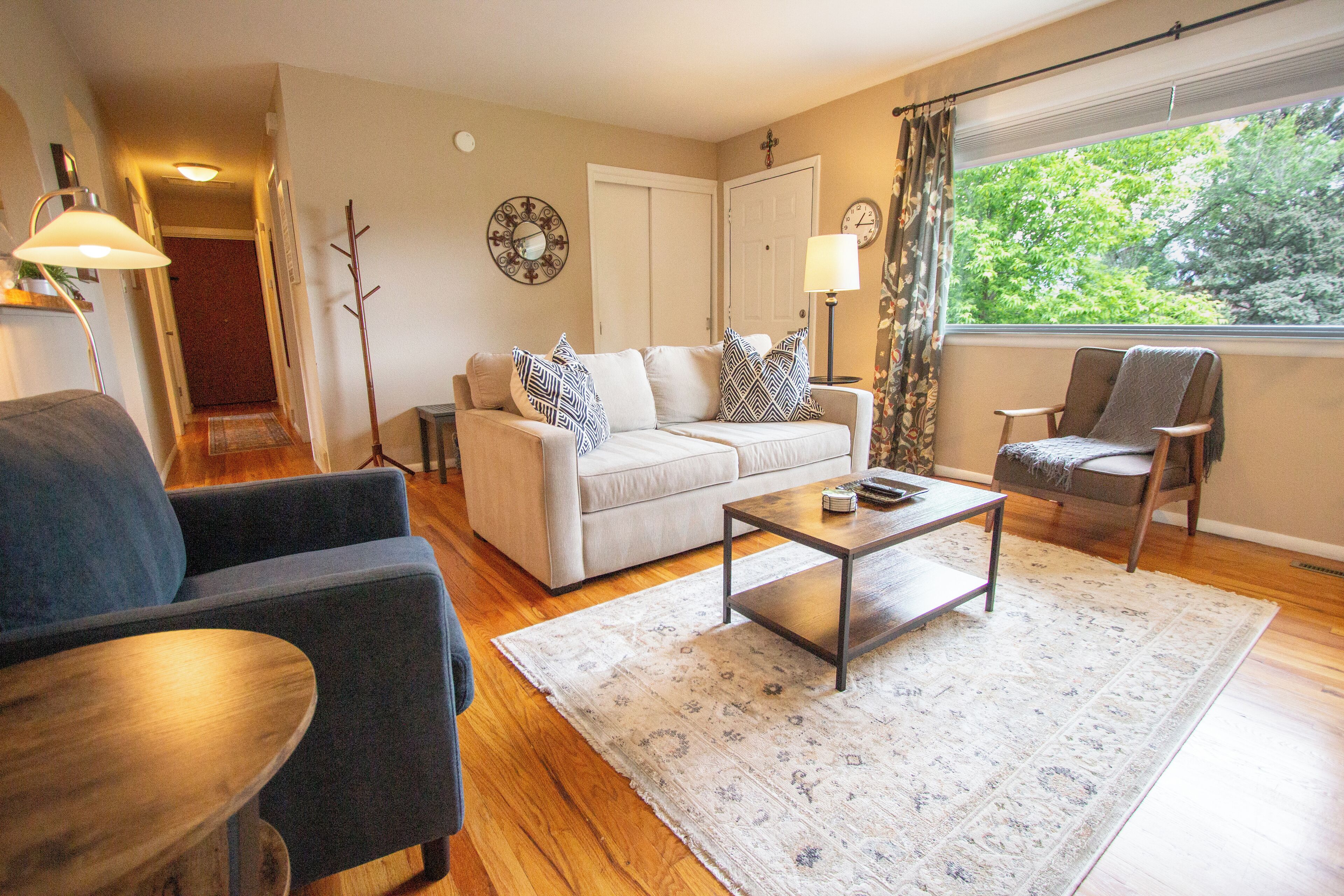 A living room with a sofa, armchairs, a coffee table, and a view of trees through a window.