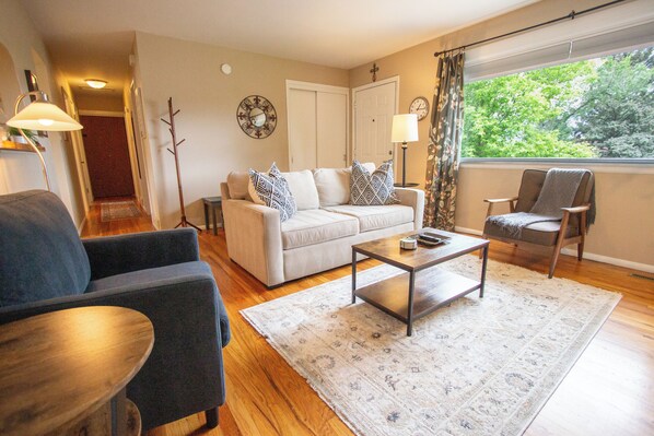 A living room with a sofa, armchairs, a coffee table, and a view of trees through a window.