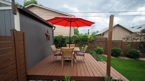 Eine Holzterrasse mit Tisch und Stühlen, einem roten Sonnenschirm und einem kleinen Garten.