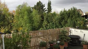 Ein Dachgarten mit Kübelpflanzen, einem Bambuszaun und einem großen schwarzen Topf.