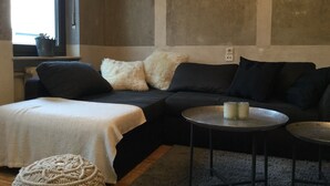A modern living room with a dark-colored sofa, a white throw blanket, a round metal table, and a textured ottoman.