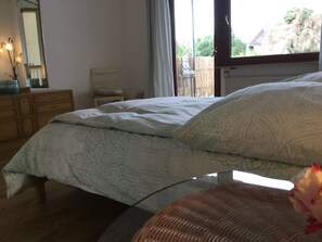 Un dormitorio con cama, tocador, silla y ventana con vistas a la vegetación.